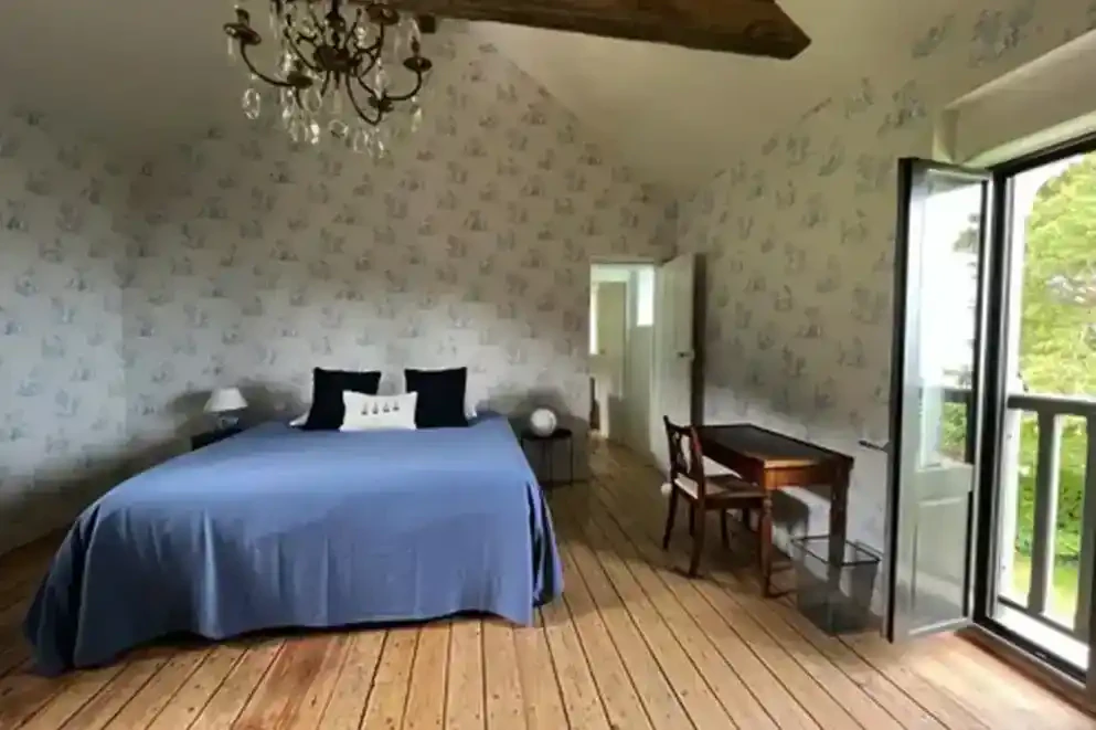 ferme-de-benerville-chambre-lit-double-bureau Chambre de la Ferme de Bénerville avec lit double, bureau et lustre élégant, décoration chaleureuse et fonctionnelle