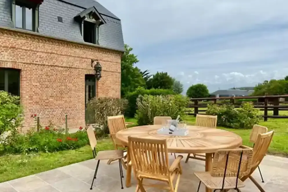 ferme-de-benerville-jardin-table-bois-facade Jardin de la Ferme de Bénerville avec table en bois et vue sur la façade de la maison, espace extérieur convivial