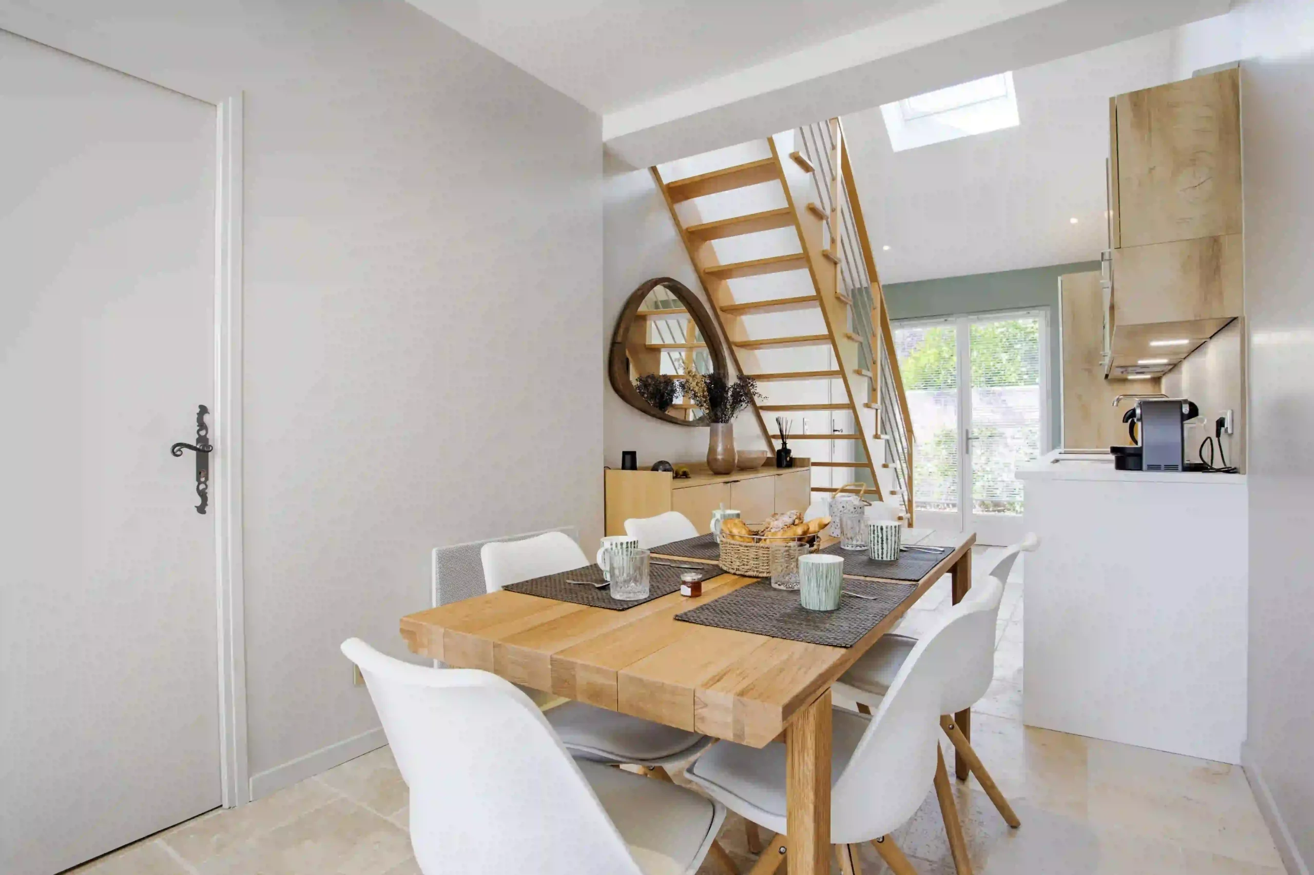 maison-le-figuier-salle-a-manger-cuisine-deauville Salle à manger de la Maison Le Figuier à Deauville avec cuisine ouverte en arrière-plan et baie vitrée laissant entrer la lumière naturelle