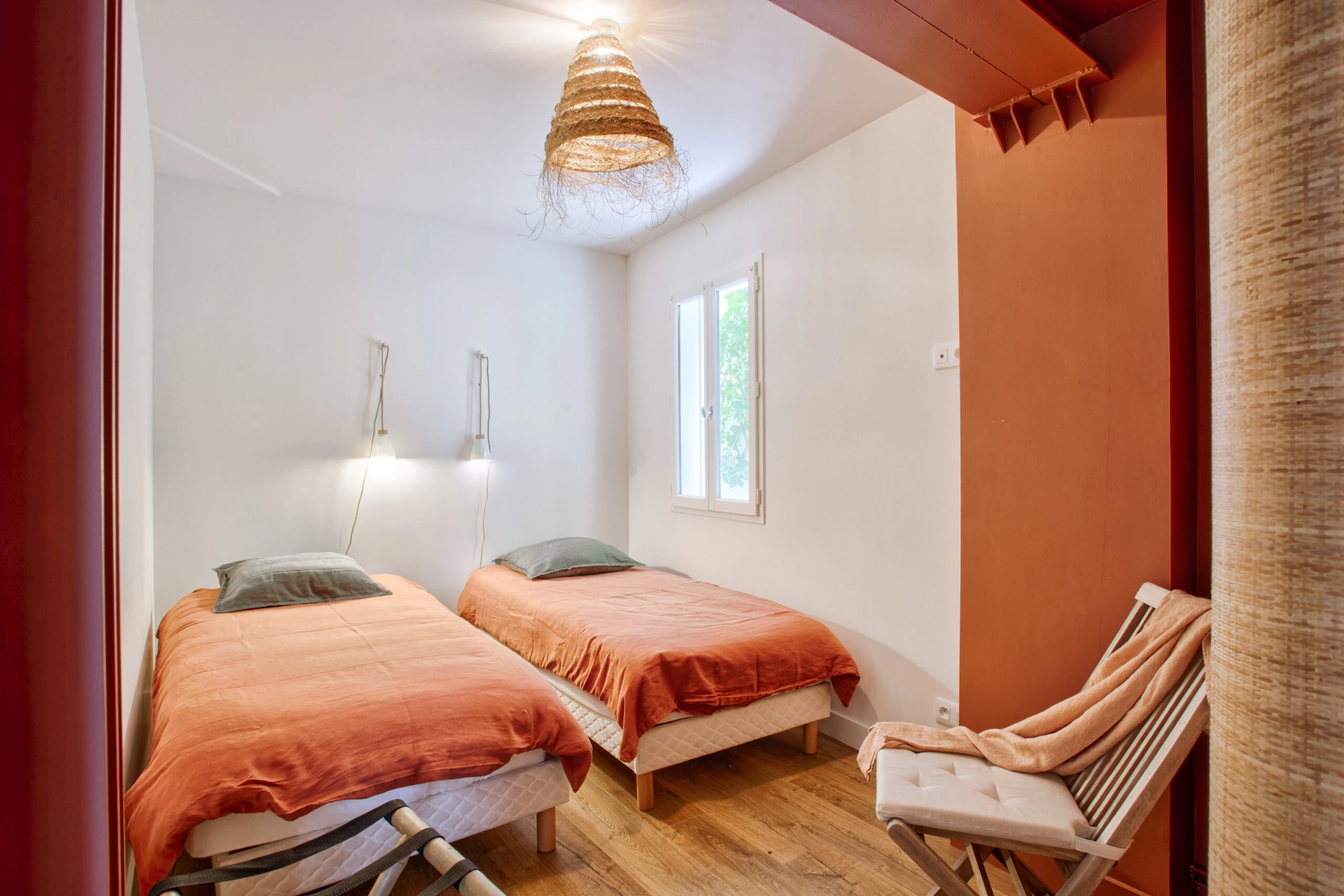 Chambre avec lits jumeaux et décoration chaleureuse – maison Laguna Chambre avec deux lits simples, linge de lit orange et décoration naturelle avec suspension en osier – maison Laguna