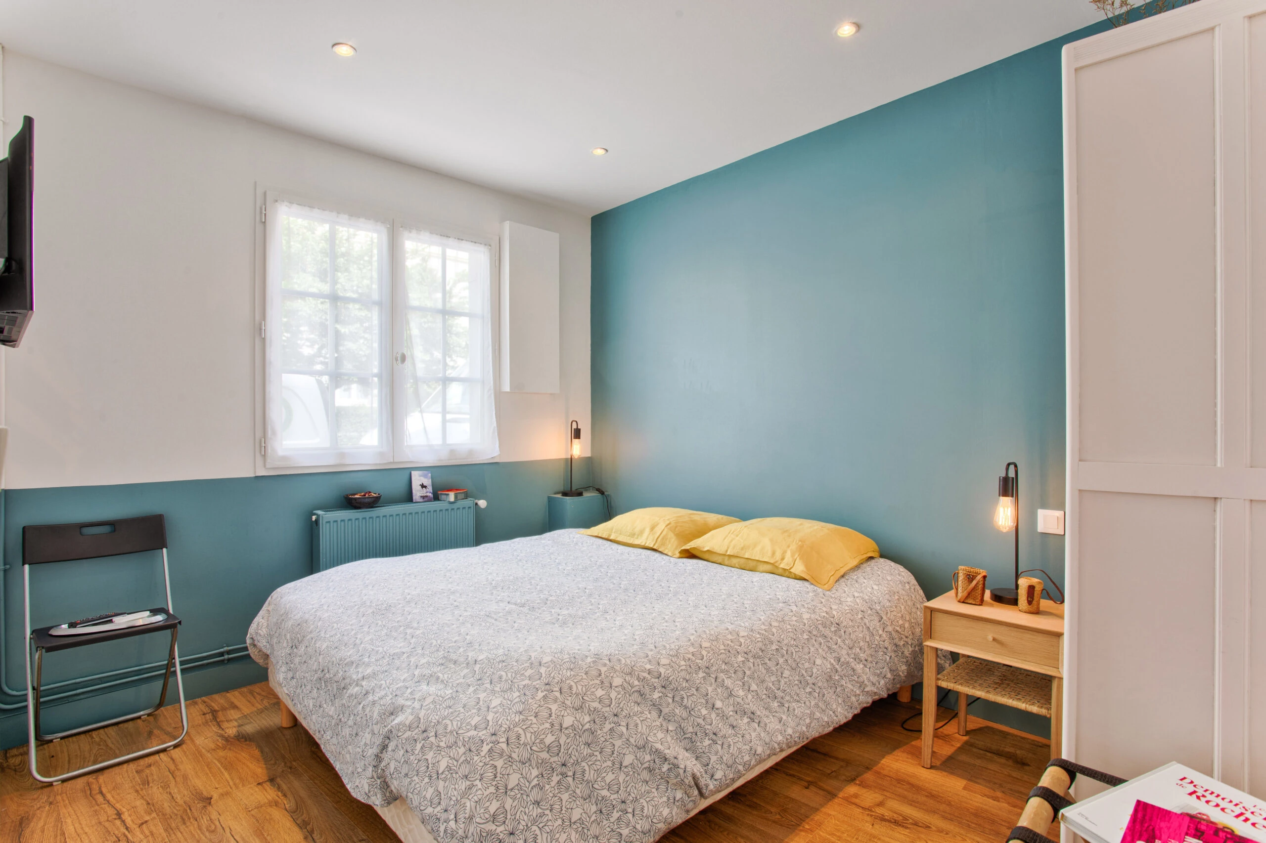 Chambre double avec mur bleu et coussins jaunes – maison Laguna Chambre double lumineuse avec un mur bleu, un lit avec coussins jaunes et une décoration épurée – maison Laguna