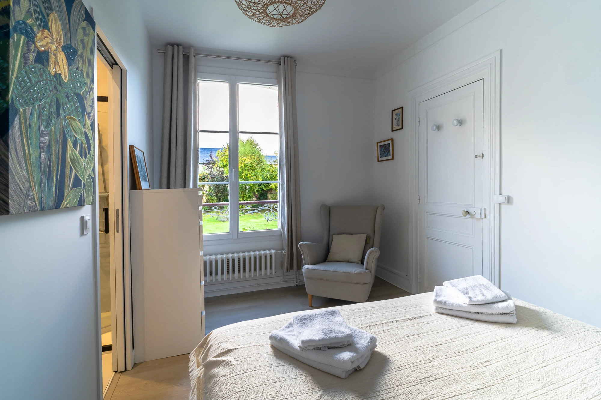 Chambre lumineuse avec vue sur le jardin – Evasion Normande Chambre cosy avec fauteuil et vue dégagée sur le jardin dans la maison Evasion Normande.