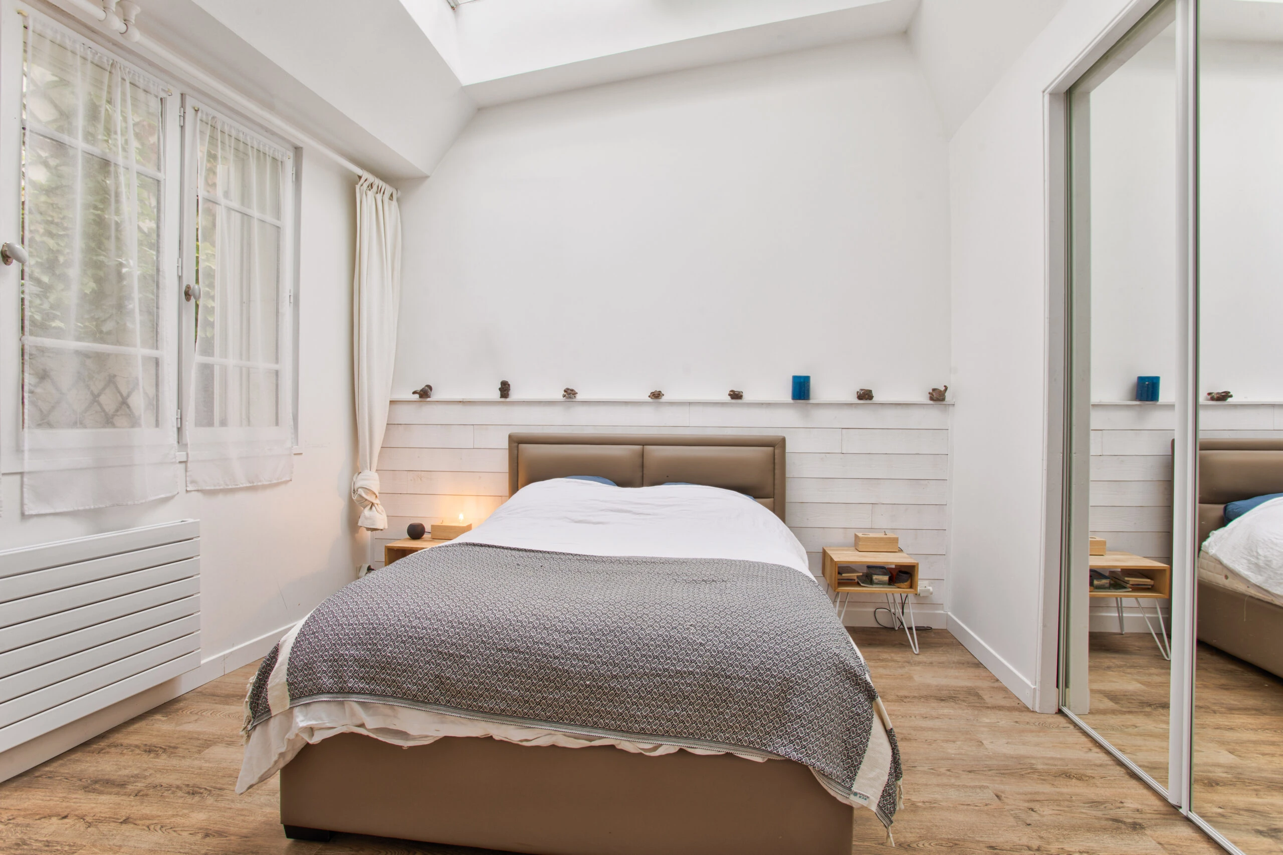 Chambre principale sous verrière avec lit double – maison Laguna Chambre double lumineuse avec lit en cuir beige, verrière et murs blancs – maison Laguna