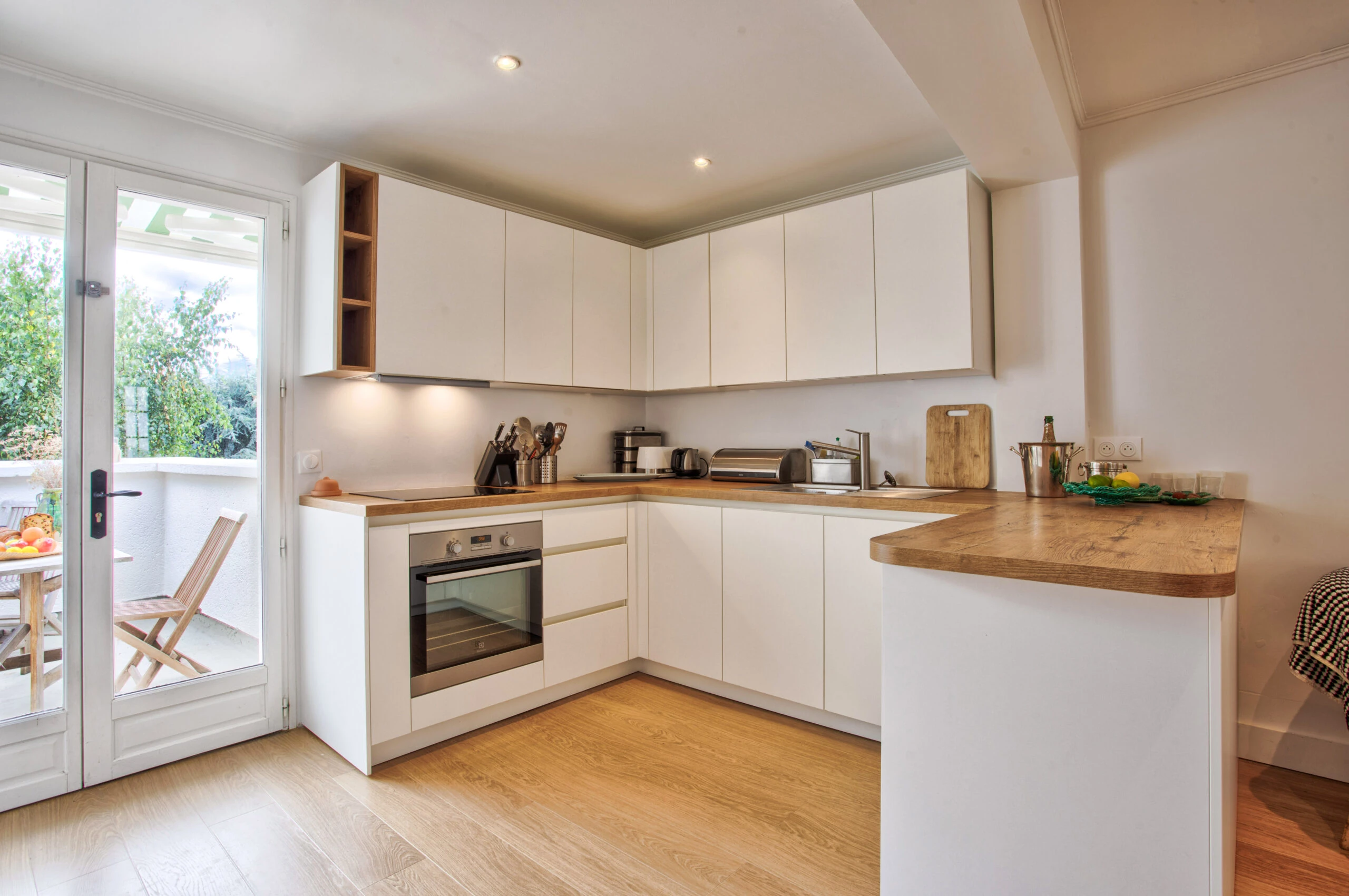 Cuisine équipée moderne avec plan de travail en bois – Maison Laguna Cuisine contemporaine avec mobilier blanc, plan de travail bois et accès à la terrasse.