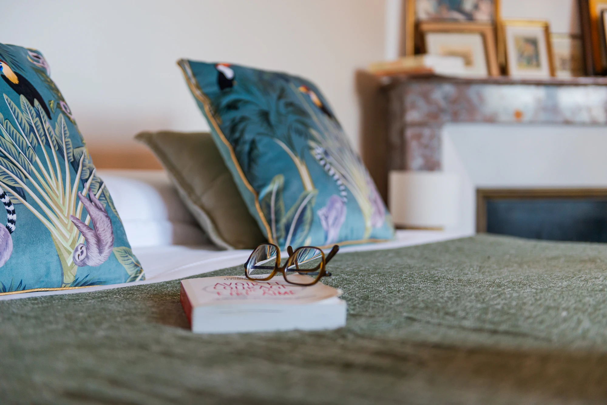 Détail décoratif chambre parentale – Evasion Normande Zoom sur un lit avec coussins décoratifs et lunettes posées, apportant une touche cosy dans la maison Evasion Normande.