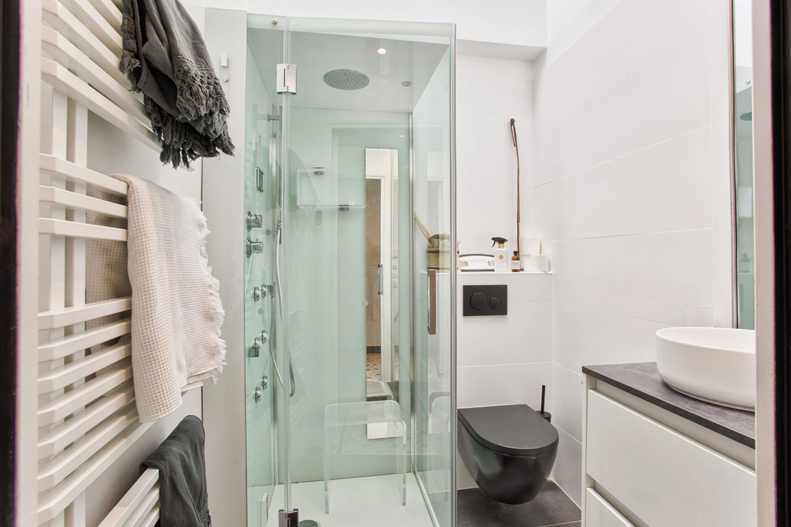Deuxième salle de bain avec douche en verre et toilettes suspendues – maison Laguna Salle de bain design avec paroi vitrée, WC suspendu noir et sèche-serviettes – maison Laguna