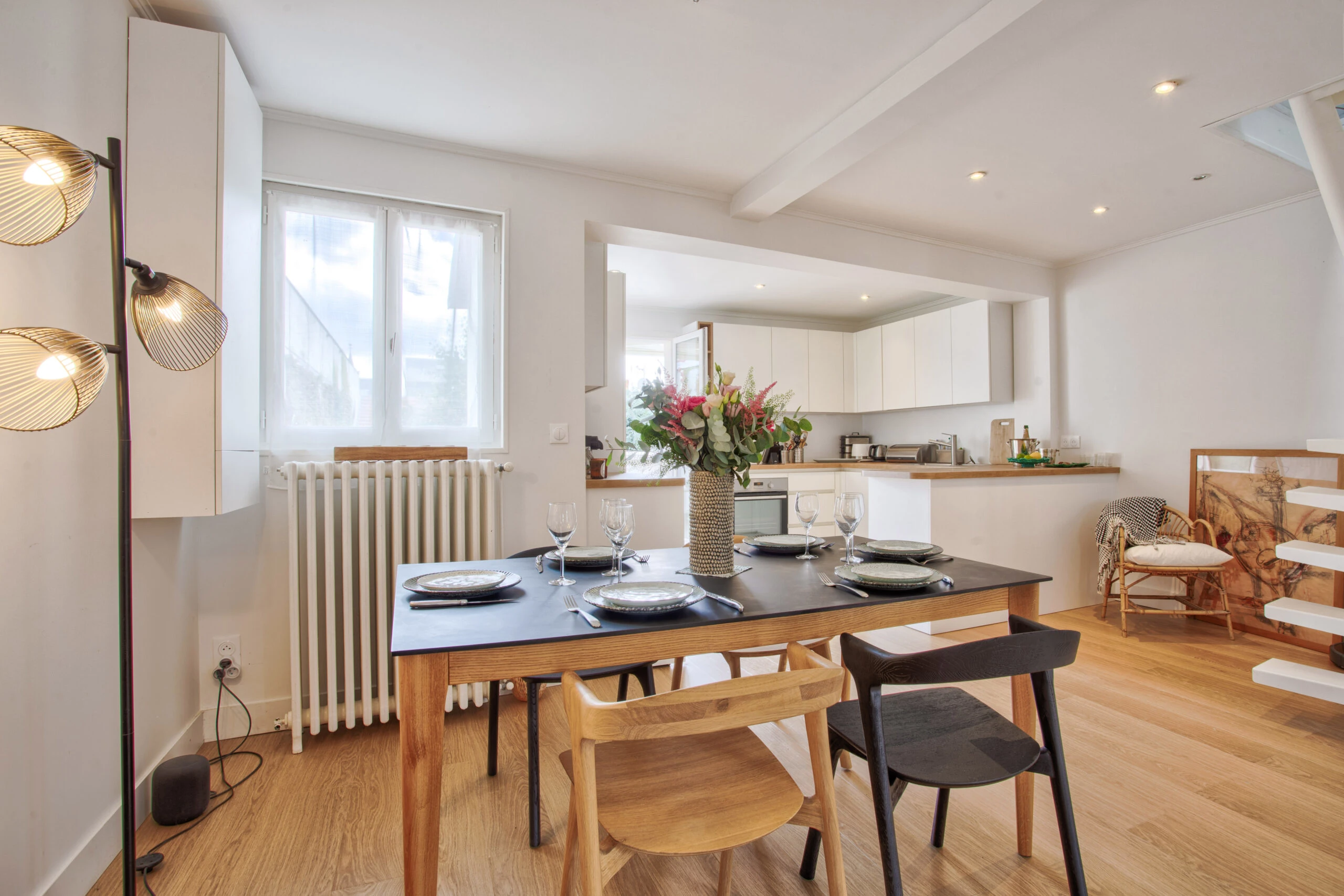 Salle à manger avec table dressée et cuisine ouverte – maison Laguna Salle à manger moderne avec table en bois et cuisine blanche ouverte, bien éclairée par la lumière naturelle – maison Laguna