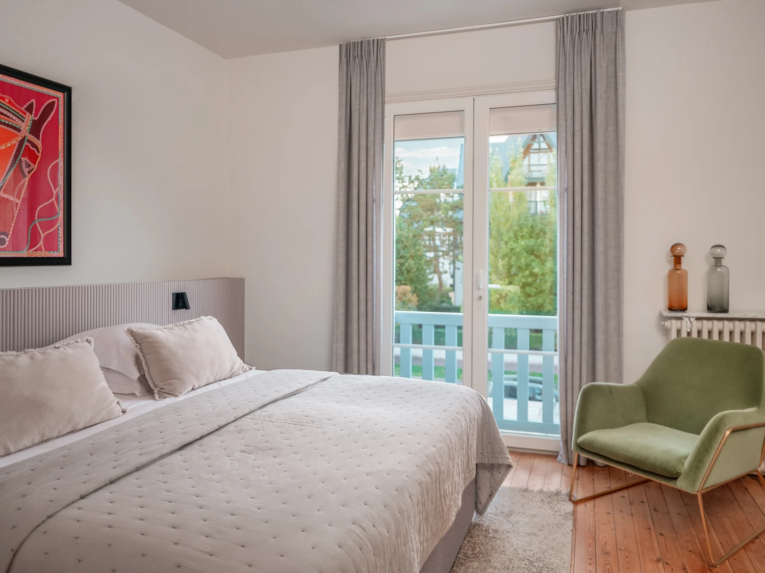 Chambre lumineuse avec balcon – Villa Berry Chambre claire avec lit double, fauteuil vert et balcon.
