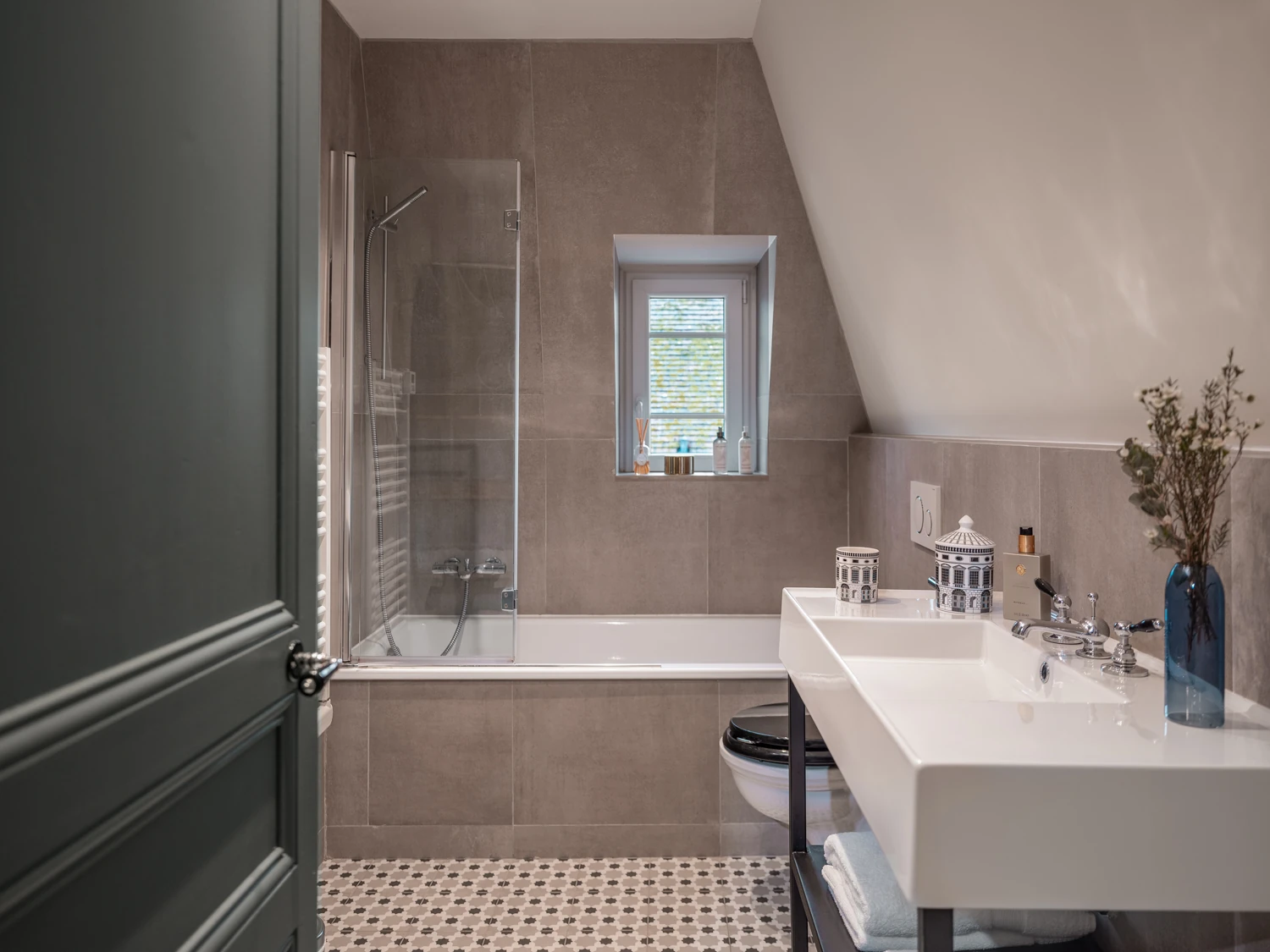 Salle de bain mansardée – Villa Berry Salle de bain sous toit avec baignoire, double vasque et carrelage graphique.