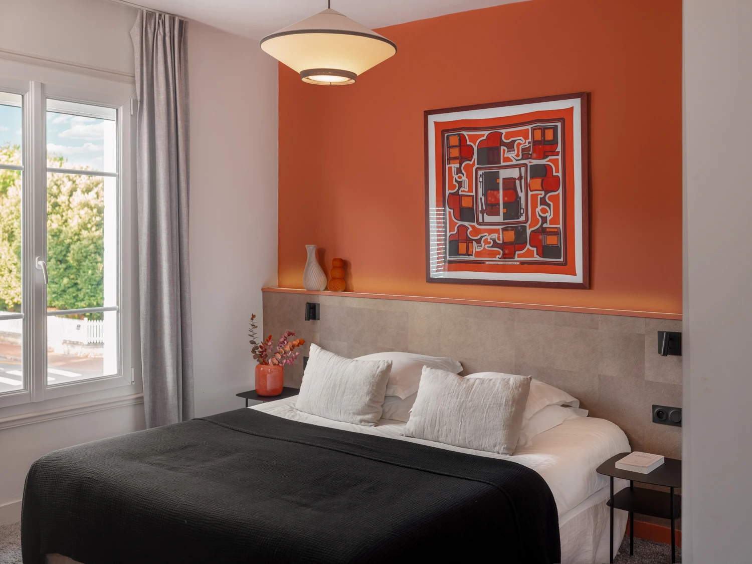Suite élégante avec tête de lit orange – Villa Berry Chambre avec mur orange, tête de lit grise et tableau géométrique.