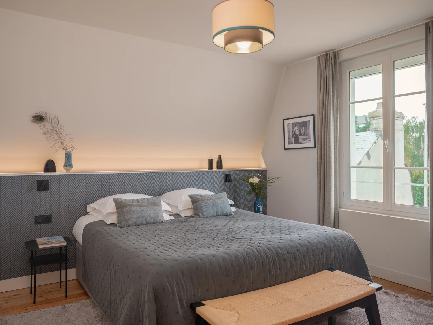 Vue frontale du lit avec fenêtre – Villa Berry Lit double avec coussins clairs et tableau rouge au mur.