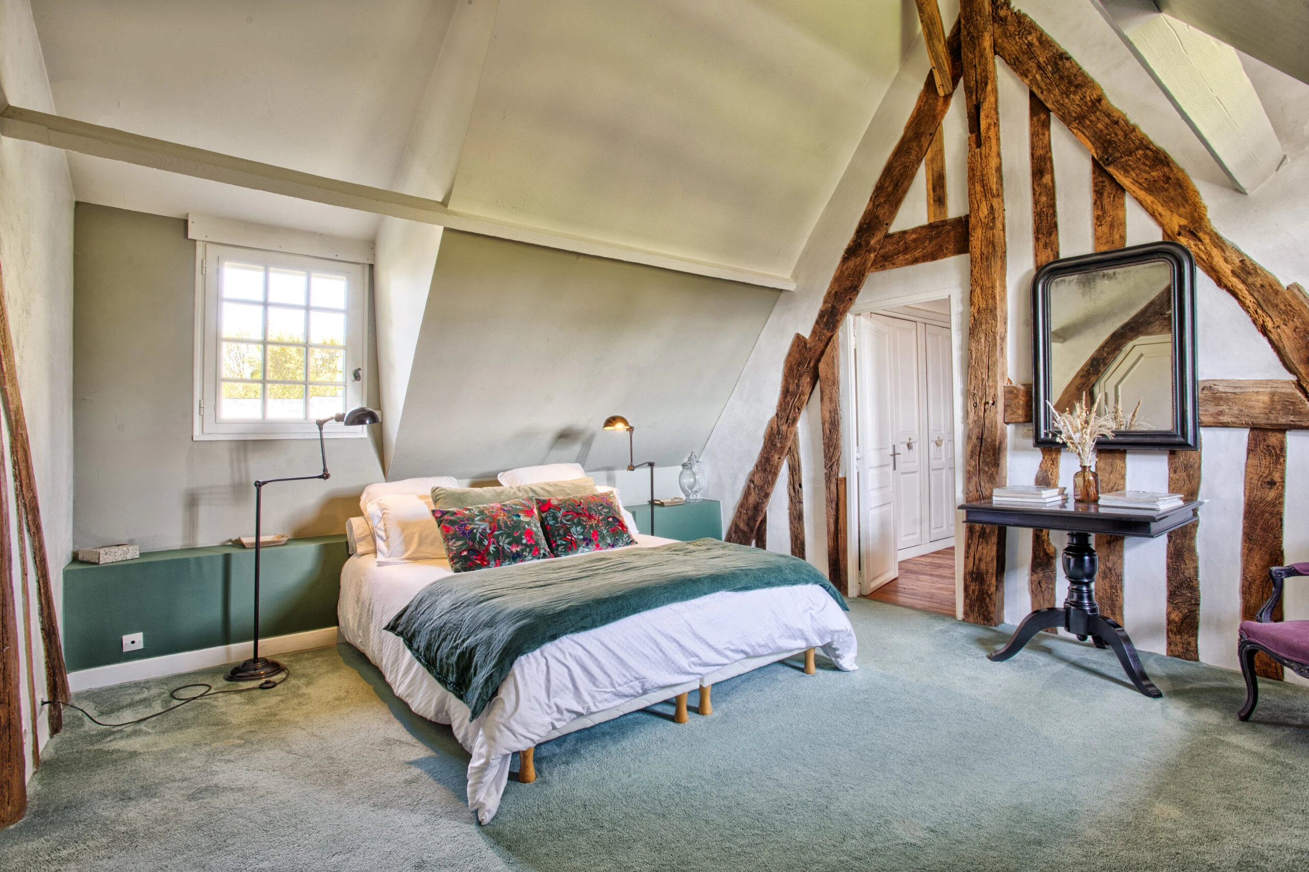 Chambre avec poutres apparentes et décoration florale – Villa Constantin Chambre spacieuse avec lit double, poutres en bois apparentes et coussins à motifs floraux dans la Villa Constantin