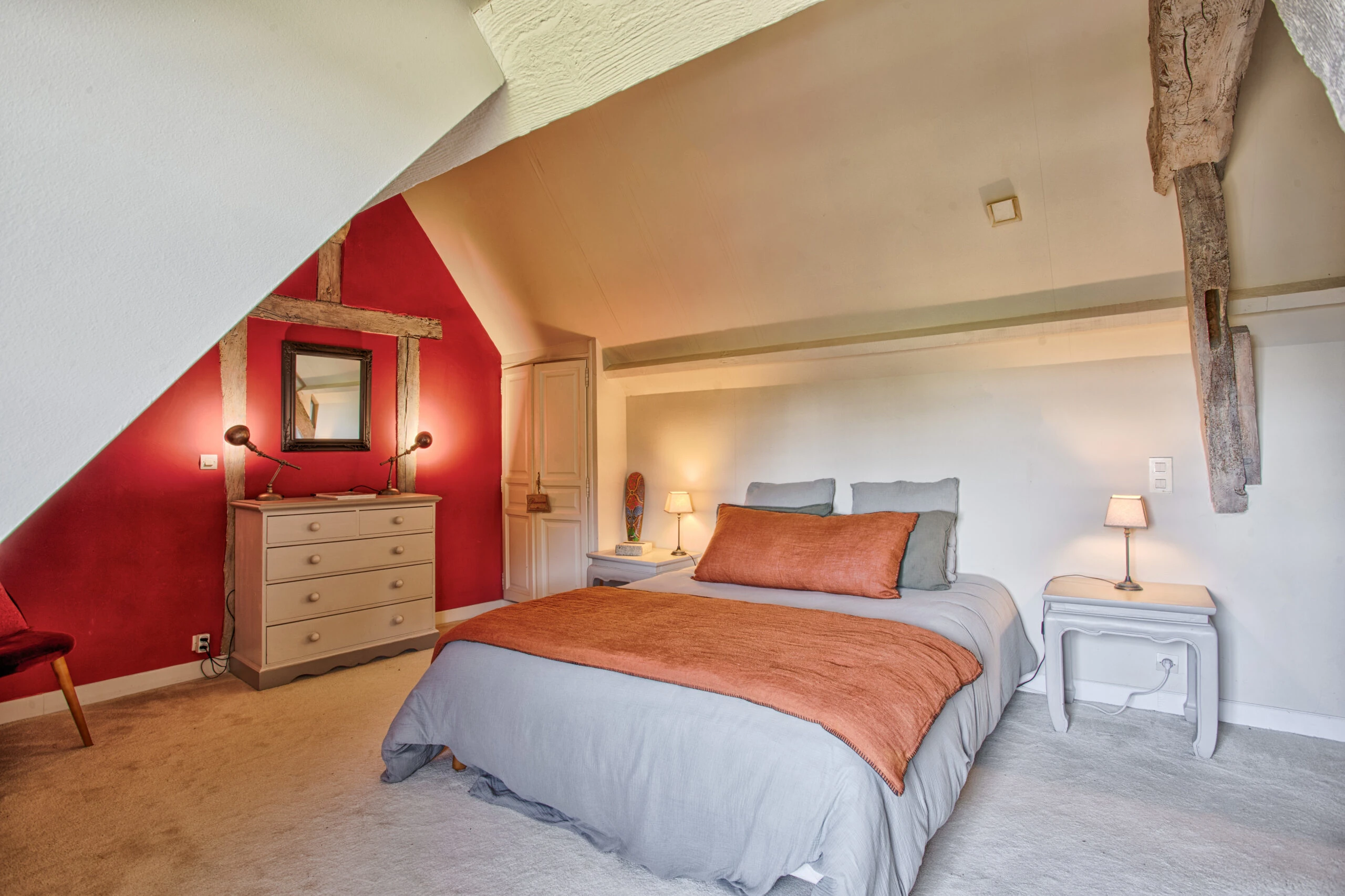Chambre cosy sous combles – Villa Constantin Chambre avec poutres apparentes, murs rouges et ambiance feutrée dans la Villa Constantin