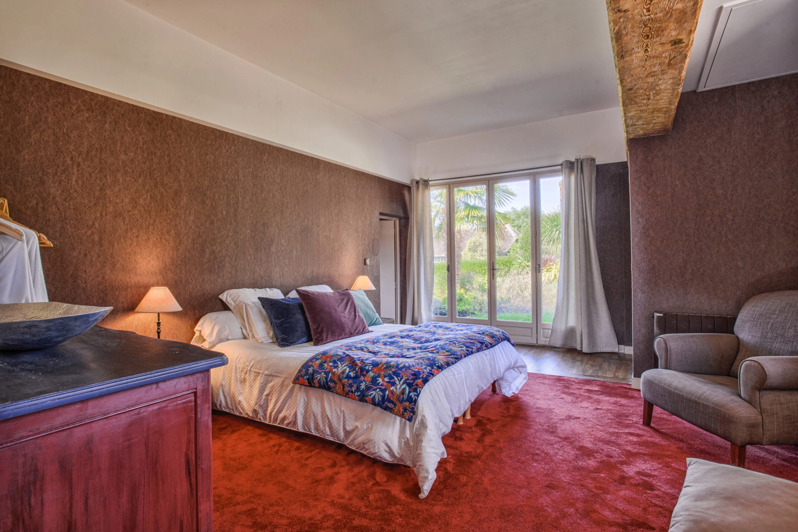 Chambre lumineuse avec vue sur le jardin – Villa Constantin Chambre spacieuse avec grande baie vitrée donnant sur le jardin fleuri de la Villa Constantin