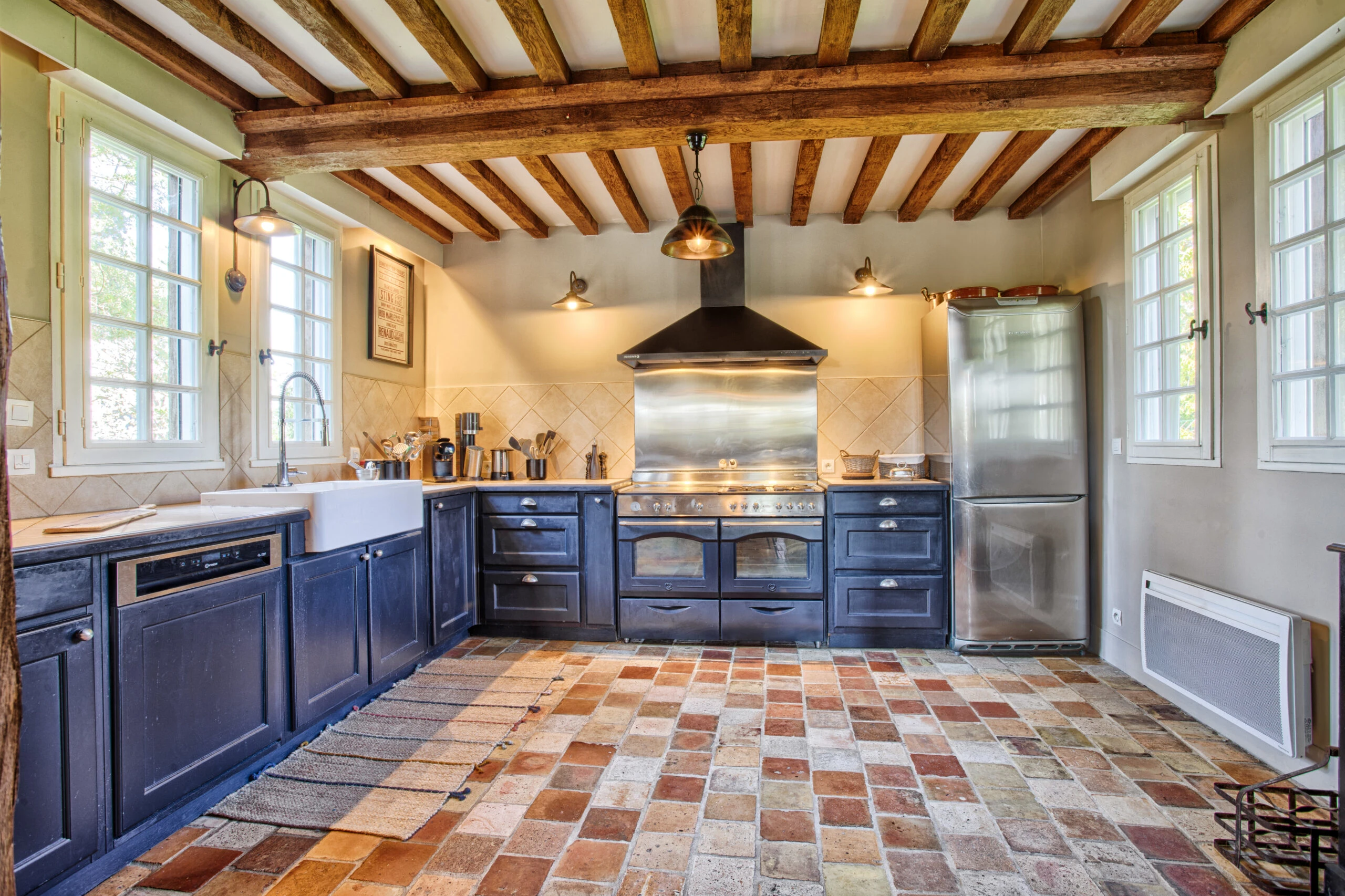 Cuisine équipée au charme normand – Villa Constantin Cuisine ouverte avec poutres apparentes, cuisinière moderne et carrelage en terre cuite dans la Villa Constantin