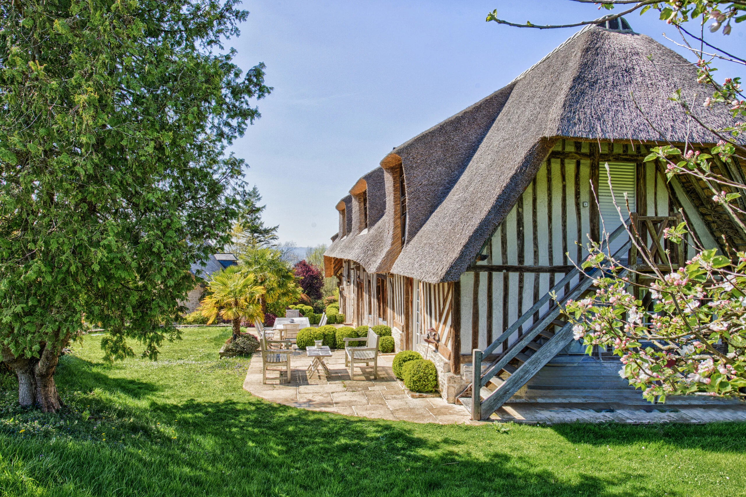 Maison normande traditionnelle avec toit de chaume – Villa Constantin Vue extérieure d’une maison à colombages avec toiture en chaume et espace détente à la Villa Constantin