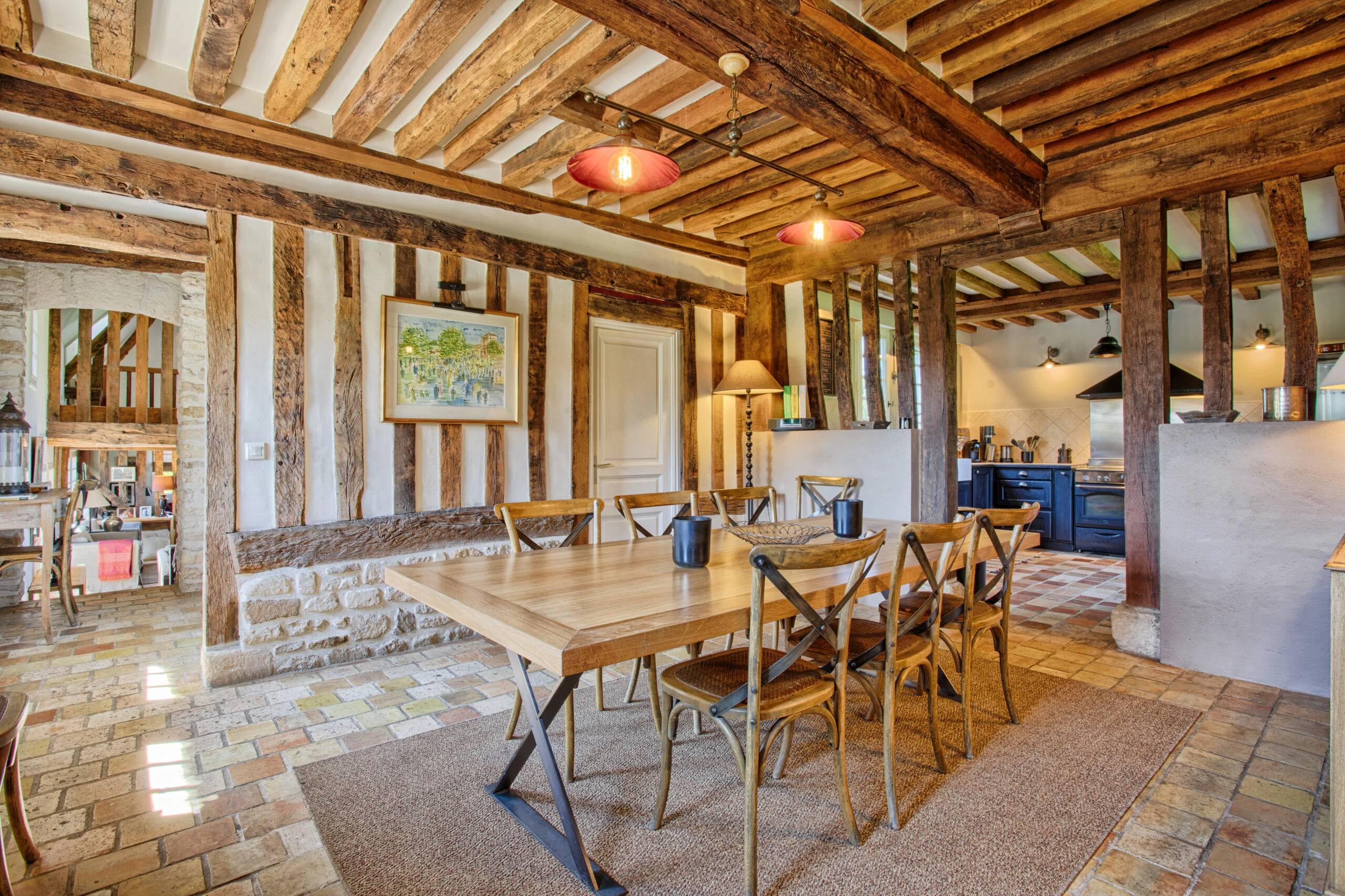 Salle à manger rustique et cuisine ouverte – Villa Constantin Salle à manger avec grande table en bois et cuisine ouverte au style normand dans la Villa Constantin