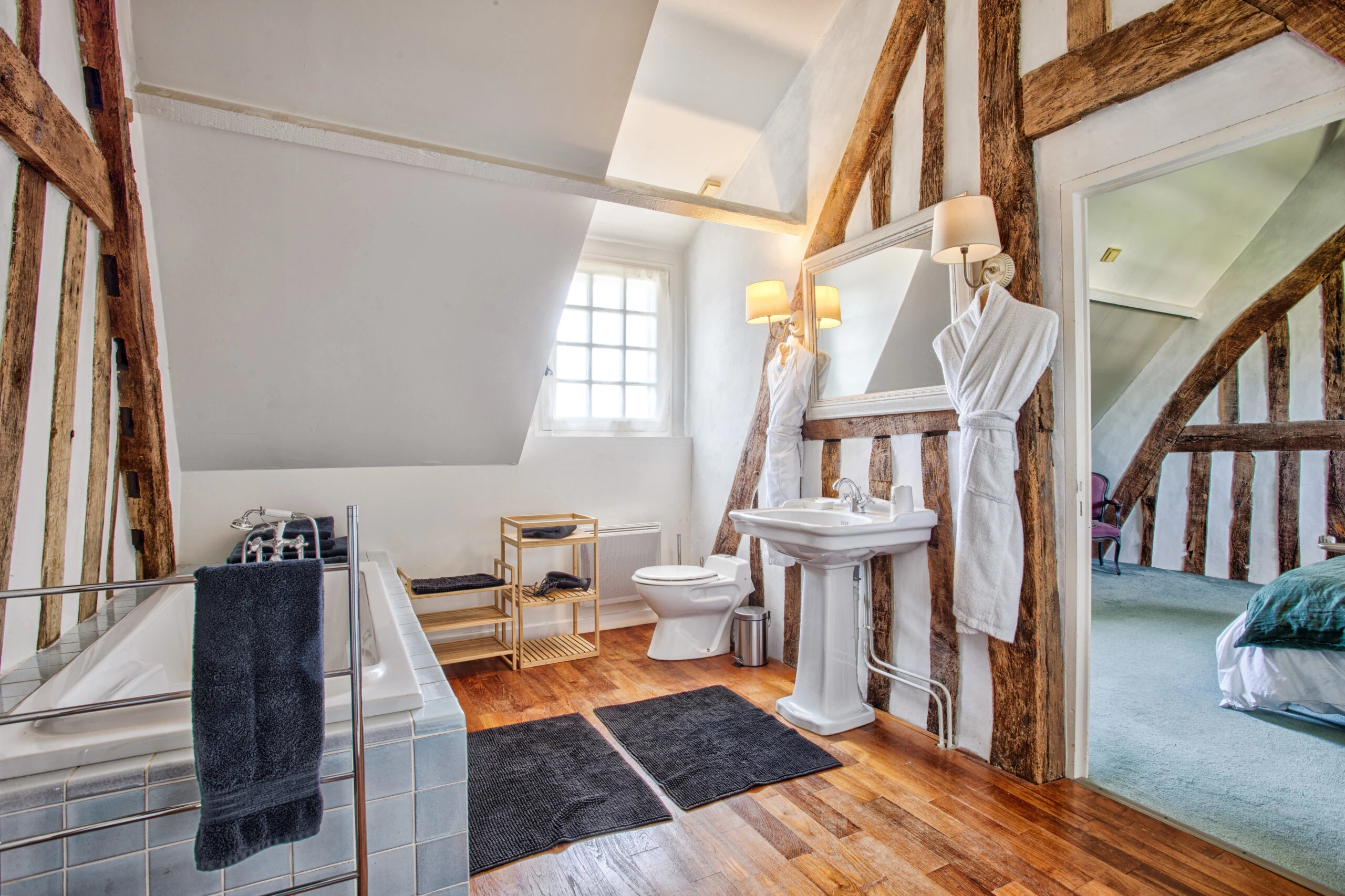 Salle de bain lumineuse avec poutres et double accès – Villa Constantin Salle de bain lumineuse avec poutres, miroir encadré en bois et double accès depuis la chambre dans la Villa Constantin