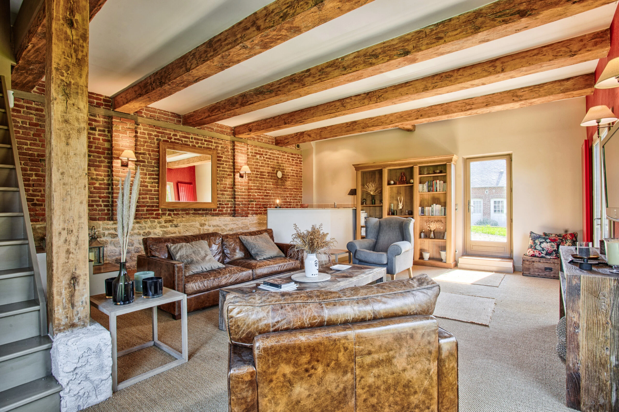 Salon élégant avec poutres apparentes et mur en briques – Villa Constantin Salon chaleureux avec poutres en bois, canapés en cuir et mur en briques dans la Villa Constantin