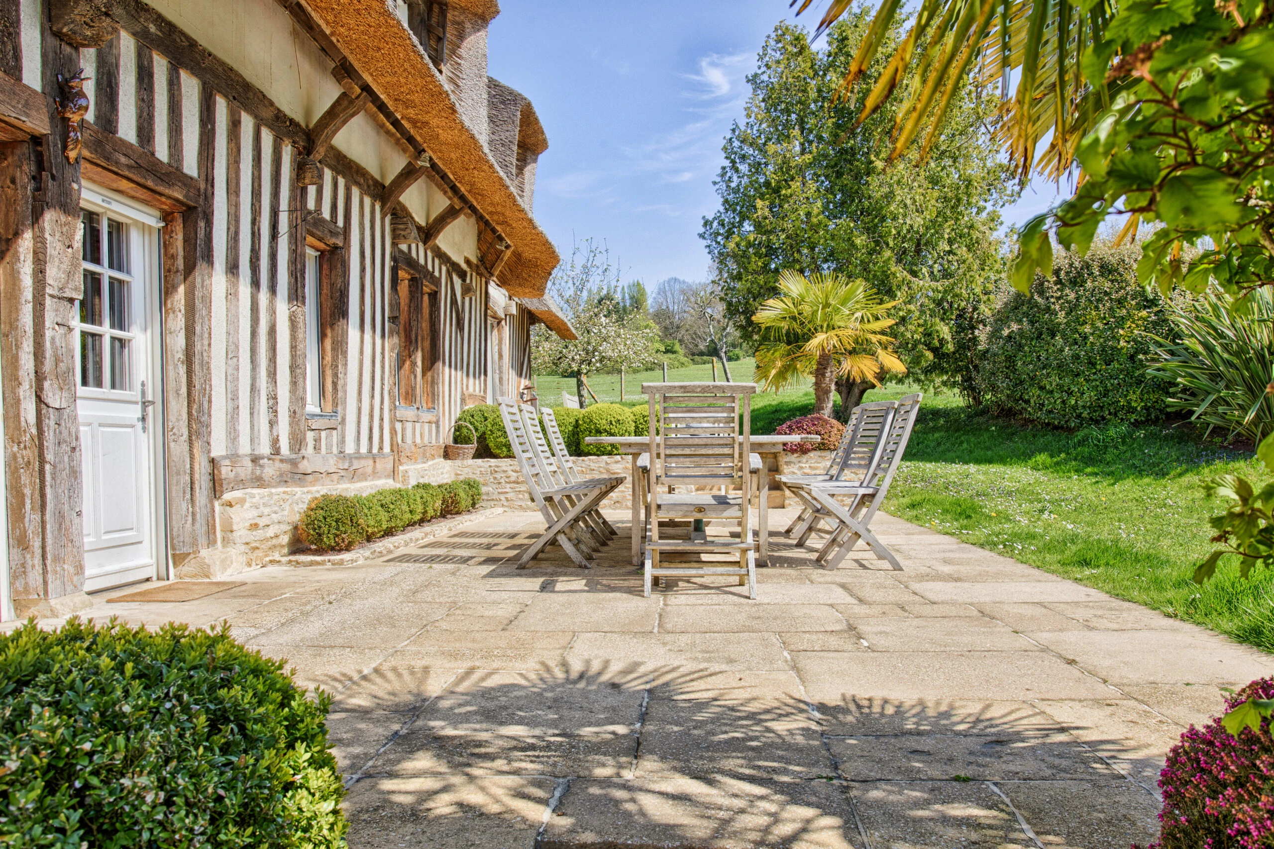 Terrasse ensoleillée avec mobilier de jardin – Villa Constantin Terrasse équipée de table et chaises en bois, entourée de verdure dans la Villa Constantin