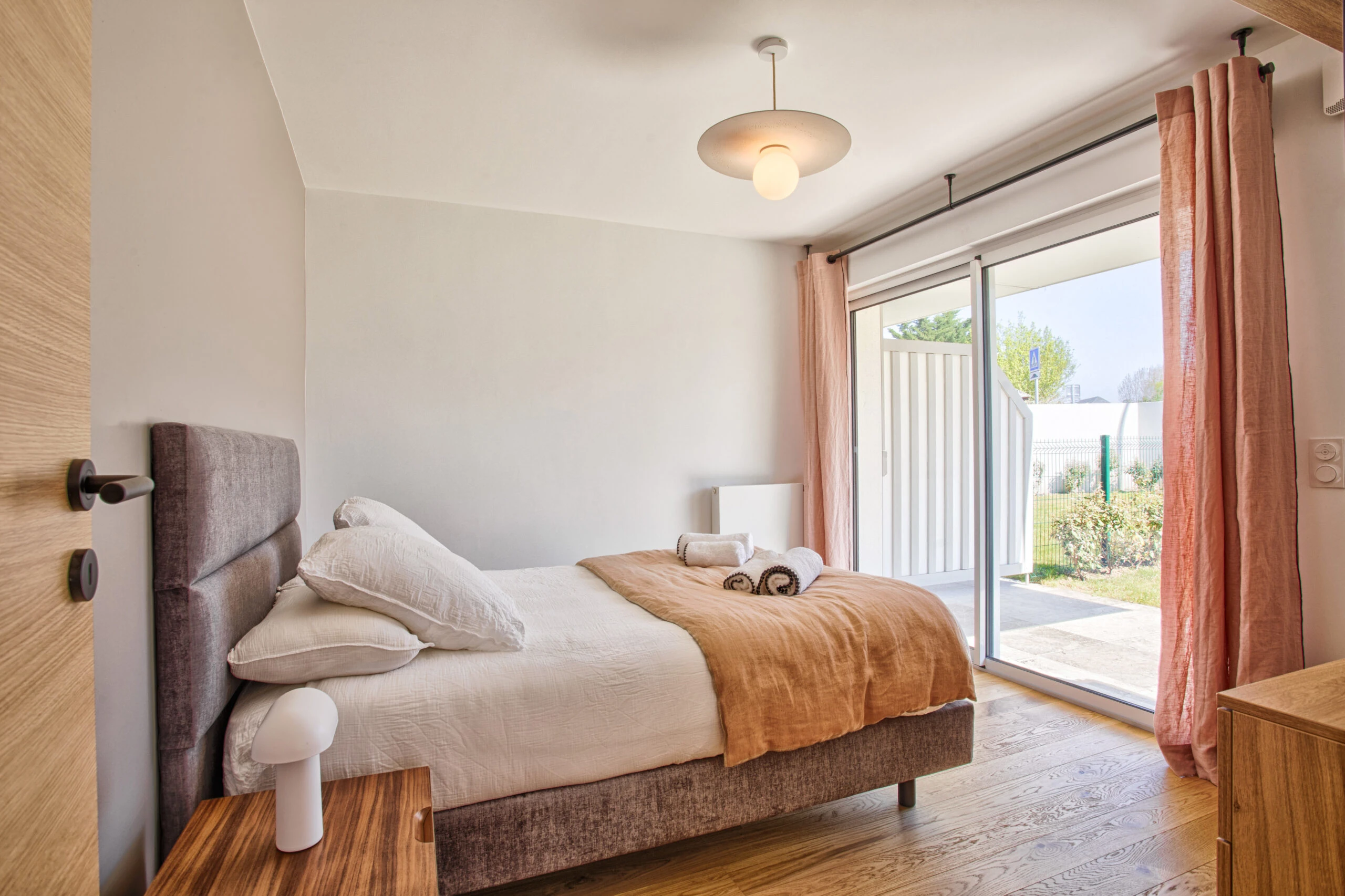 Chambre avec accès extérieur – Studio Un singe en Hiver Lit double avec draps beige, grande baie vitrée donnant sur le jardin