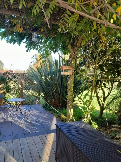 Coin détente sous pergola végétalisée – Les Glycines Pont l’Évêque Petit coin repas à l’ombre d’une pergola végétalisée dans le jardin du logement Les Glycines.