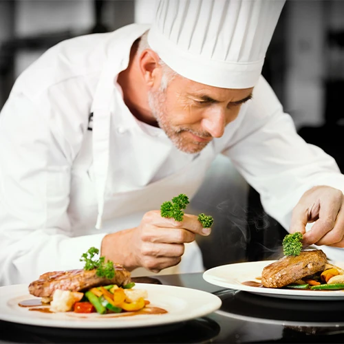 Chef professionnel en train de dresser des assiettes gastronomiques, symbole du service de restauration privée offert par la conciergerie
