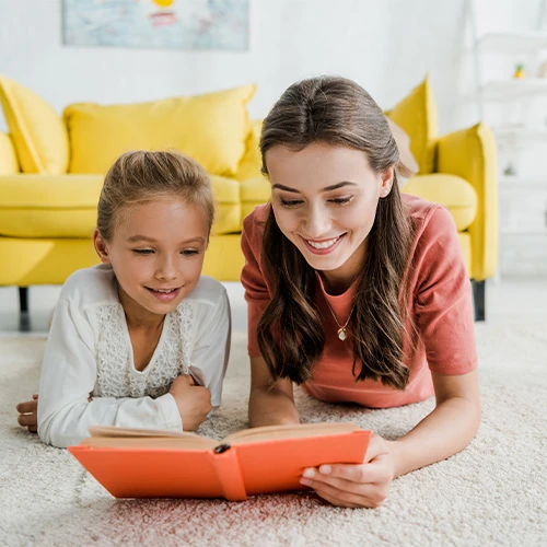 Jeune femme lisant un livre avec une enfant dans un salon lumineux, illustrant un service de garde d’enfants à domicile proposé par la conciergerie privée