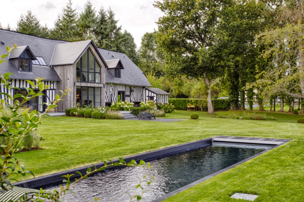 Vue extérieure d’une villa normande haut de gamme avec bardage bois, jardin arboré et piscine moderne, à Deauville