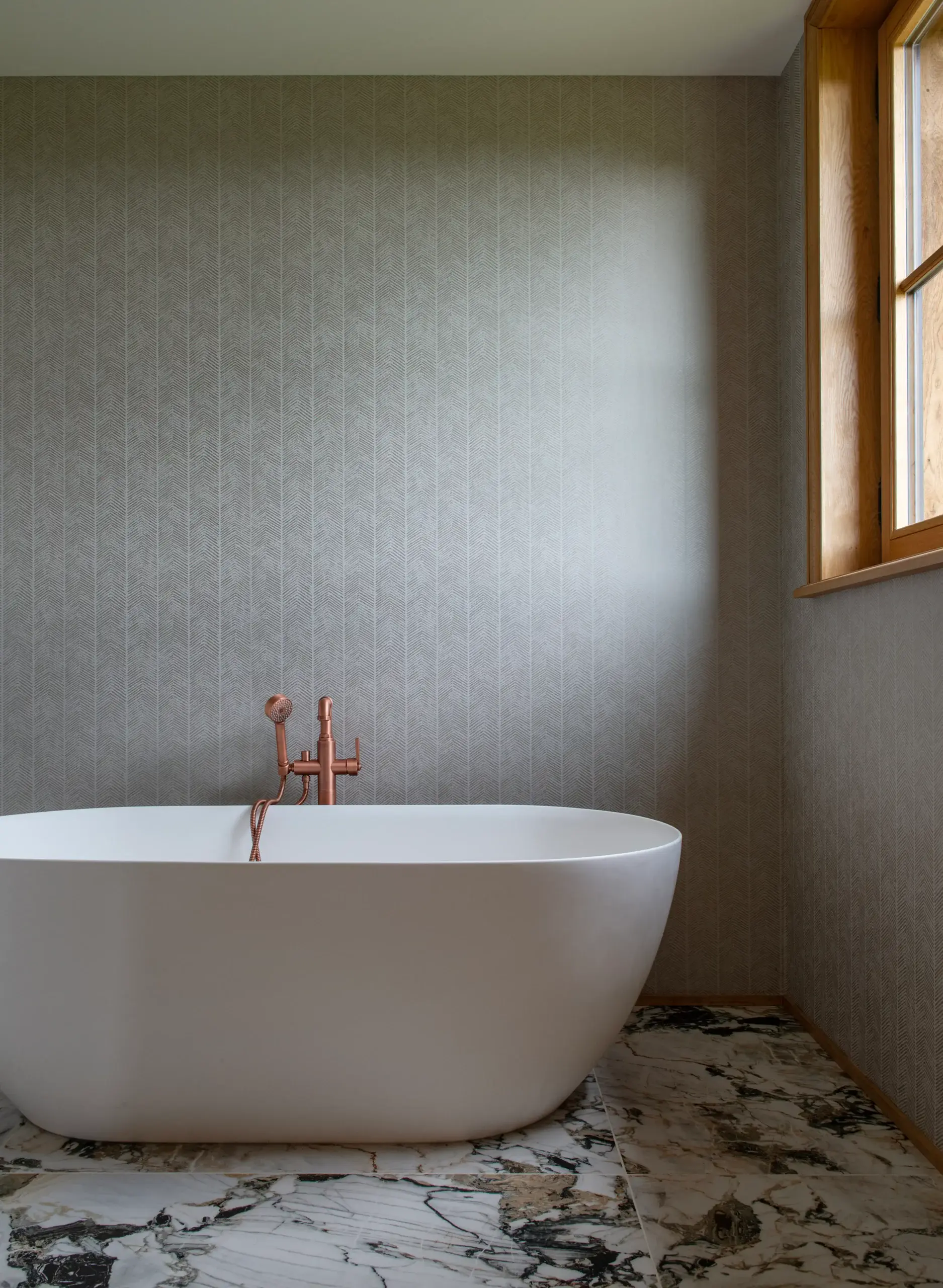 Dortoir - salle de bain Baignoire îlot en solid surface avec robinetterie cuivrée sur sol en marbre veiné dans une demeure de prestige gérée par conciergerie de luxe en Normandie