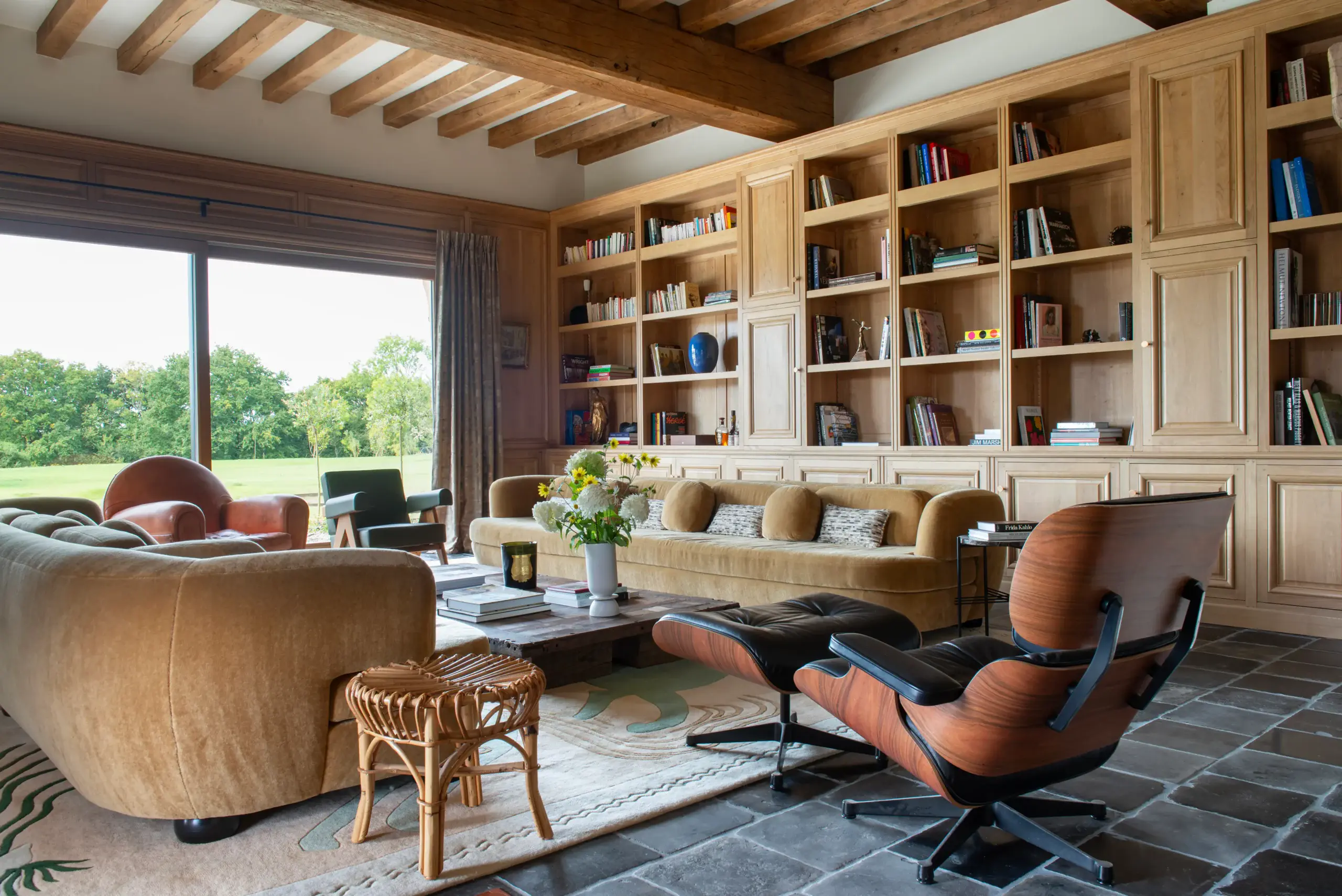 Salon vue extérieur Salon spacieux avec Eames lounge chair, bibliothèque en chêne et vue panoramique sur parc dans une demeure gérée par conciergerie de luxe en Normandie